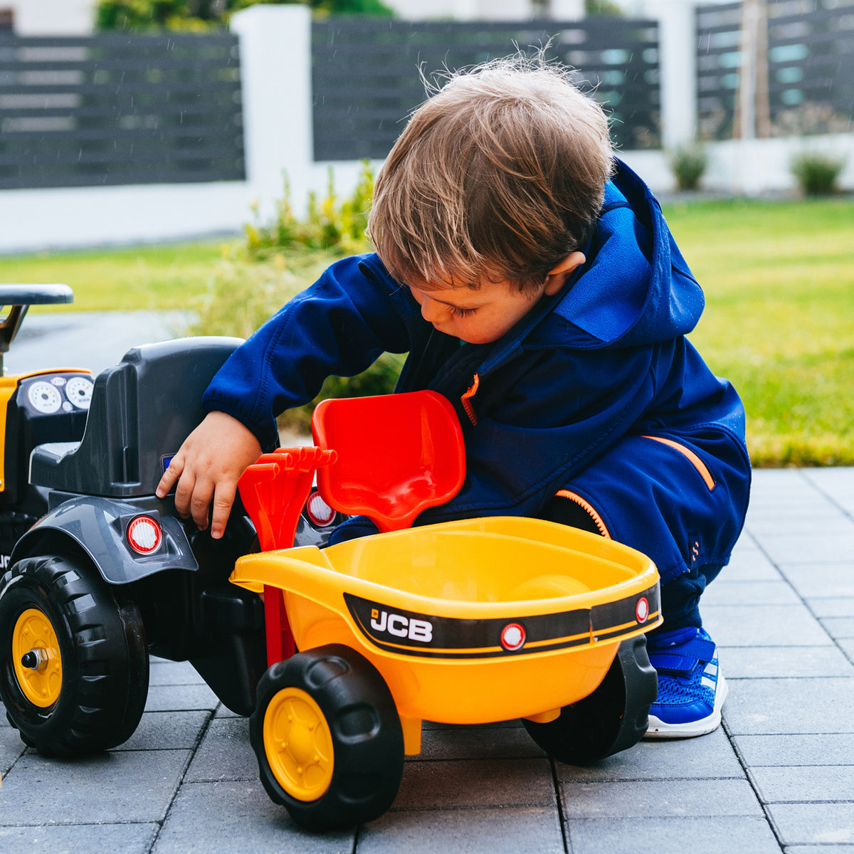 Oranžs JCB traktors ar lāpstiņu un grābekli piekabē