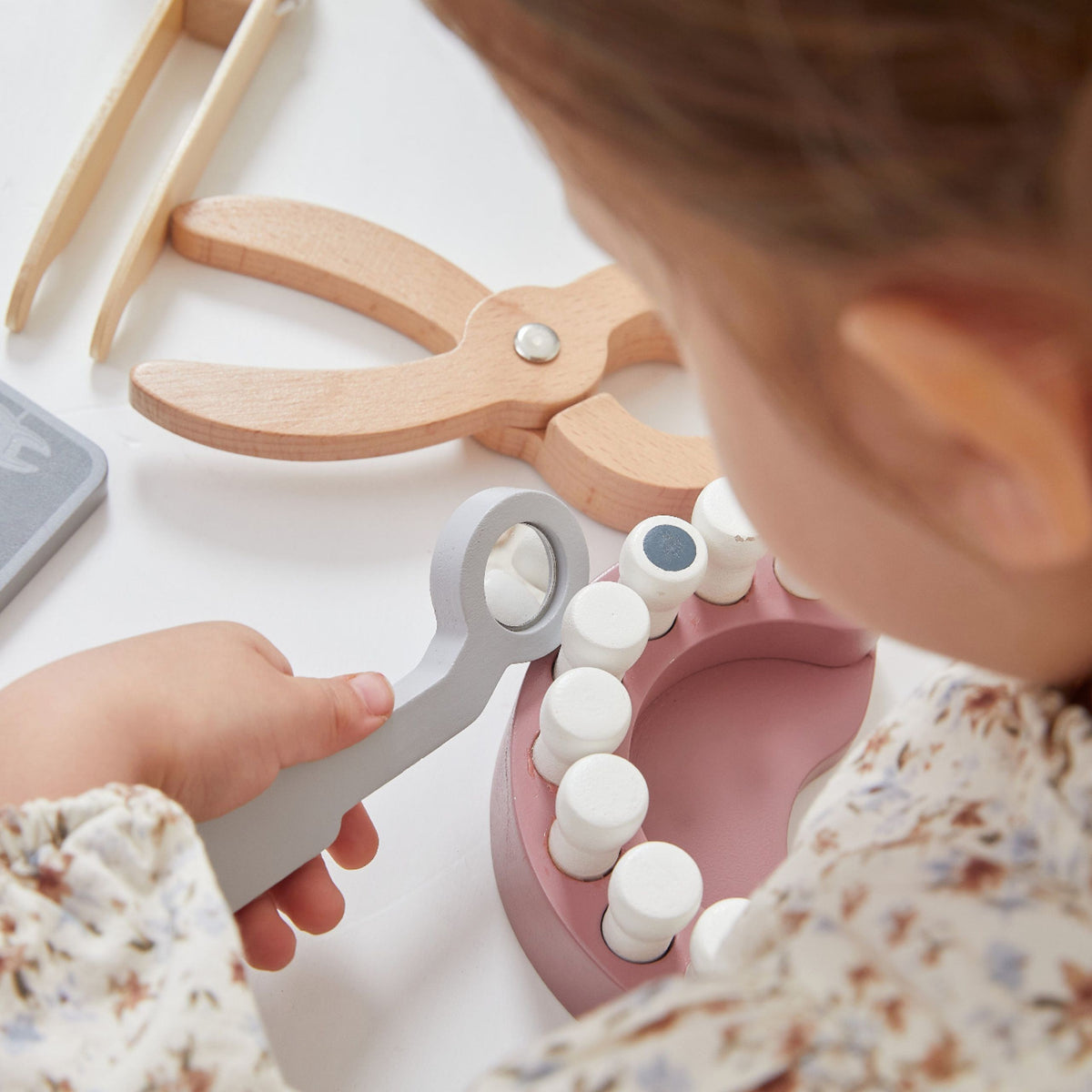 Child playing dentist with the wooden mirror