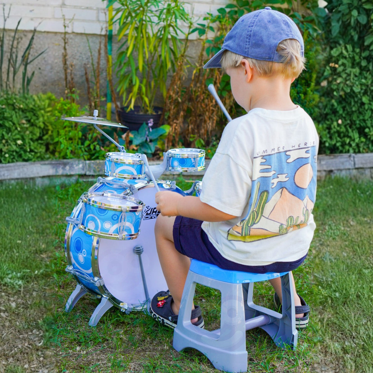 Child playing the blue toy drum kit on the stool